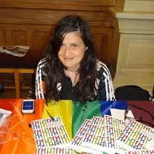 portrait de Brigitte Brami, assise derrière une table avec un drapeau arc en ciel dessus.